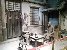 Model of a Chinese dwelling with clay models of two men sitting at a table in conversation