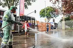 Washing and disinfection of the street during the COVID-19 pandemic with overalls, gloves, mask, and protective boots as protection against biohazards.