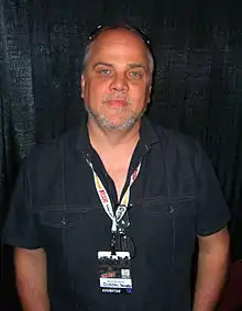 Man with a goatee, wearing a black short-sleeved shirt