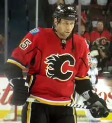 Upper body of a man staring intently into the distance.  He is in a full hockey uniform; the jersey is red with black and yellow trim, and a black stylized "C" logo on his chest.