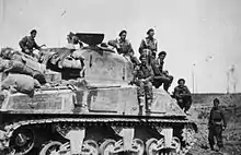 A black and white photograph of a tank; several men in military uniforms are posing standing on the tank