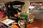 A green-colored, old-fashioned car with four seats and brass fittings