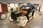 A green-colored, old-fashioned car with four seats and brass fittings