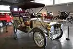 A white-colored, old-fashioned car with four seats and brass fittings