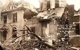 Black-and-white photograph with beige tint showing downed tree limbs and wrecked roofs