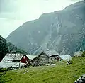 1960.  Sinjarheim is situated at the edge of a precipice where the bottom of the abyss was filled with the foaming Aurlandselvi.  Due to this it was common practice to secure the children with ropes.  The trees in the background to the left are on the other side of the valley.  The mountain in the background is Eisingaberget where cattle drives were led before the passage in Sinjarheimsgalden was built and passable for cattle drives in 1870.