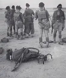 Seven soldiers only one facing the camera, wearing hot climate uniform, in a desert type terrain