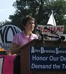 O'Neill speaking at a lectern outside in 2005 amongst lots of signs, NOW logo visible behind her