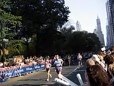 Three runners in a race down a street where onlookers are cheering behind barriers.