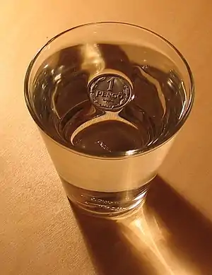 Surface tension prevents a coin from sinking: the coin is indisputably denser than water, so it must be displacing a volume greater than its own for buoyancy to balance mass.