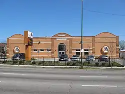 A large brick building behind black gates with and a parking lot with several parked cars