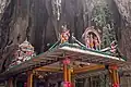 Four-pillared structure with religious statues on the roof in front of a rock wall inside the cave.