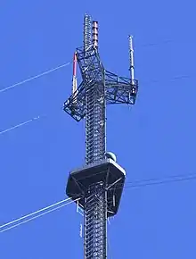 Closeup of a tall gray television tower with a candelabra shape holding three antennas