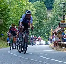 Riders cycling in a line up a street on a forested hill