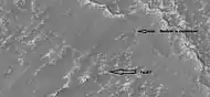 Close-up of a cliff showing possible faults, as seen by HiRISE under HiWish program; note the rock that seems to be split by the fault.  Some boulders are sitting in round holes because their ability to gather and hold heat may have melted ground ice.