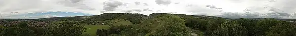 Hills covered with green vegetation. To the left in the distance are houses and water. Ahead is exposed rock.