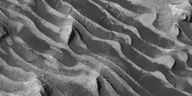 Close up of layers in Danielson Crater, as seen by HiRISE under HiWish program—boulders are visible, as well as dark sand