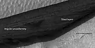 Close view of wall of triangular depression, as seen by HiRISE layers are visible in the wall.  The lower layers are tilted, while layers near the surface are more or less horizontal.  Such an arrangement of layers is called an  "angular unconformity."