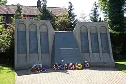 Grey-brown monument in the shape of a dam, with floral wreaths at its base