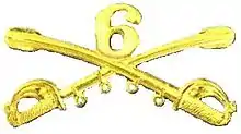 A computer generated reproduction of the insignia of the Union Army 6th Regiment cavalry branch. The insignia is displayed in gold and consists of two sheafed swords crossing over each other at a 45-degree angle pointing upwards with a Roman numeral 6