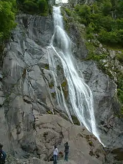 A large waterfall tumbling 37m (120 feet) over grey igneous rock, with people below observing it.