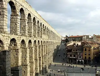 A stone aqueduct bordered by a modern road and smaller houses.