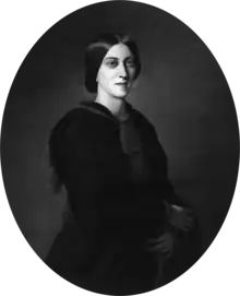 Three-quarter oval portrait of a slender woman aged about 30, garbed in black. Her deep-set eyes gaze solemnly over the viewer's shoulder. Her dark, straight hair is parted in the centre without a fringe, combed over the ears, and pulled back in a low bun.