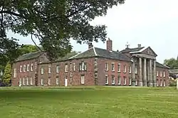 A brick house with stone dressings seen from an angle; a prominent portico is on the south front