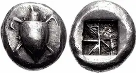 Both sides of a silver coin.  One side has a relief of a turtle; the other the impression of a square divided into eight segments.