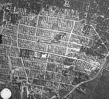 An aerial photograph of the former Warsaw Ghetto area, showing the camp's structure (a long and narrow rectangle in the image's centre) surrounded by Warsaw Ghetto's ruins