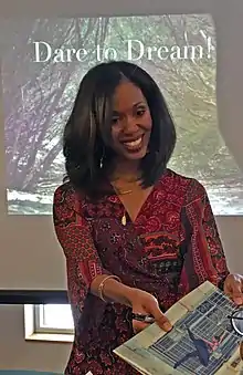 Aesha Ash signing photos in front of a screen that reads "Dare to Dream"