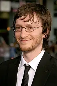 A profile picture of a blonde man who is smilling. He wears glasses and tuxedo.