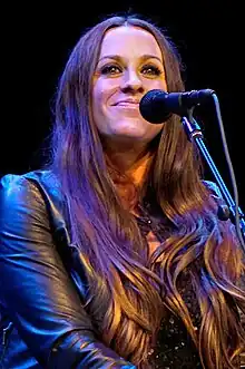 Alanis Morissette sits smiling at the camera