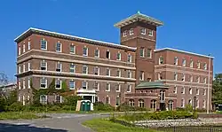  A brick building with two offset wings and a higher tower in the center with a peaked green top