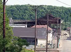 A color photograph of a building, with a forested ridge in the background and power lines in the immediate foreground