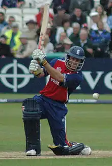 Cricketer in red and blue down on one knee while playing a shot