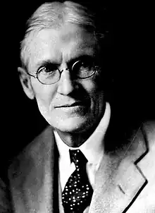 Black and white head-and-shoulders photo of silver-haired Andrew Sledd in glasses, suit jacket and tie