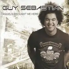 Upper body shot of a 22-year-old man. He is at the right, wearing a dark tee-shirt. The artist's name is written in large letters across the top and partly obscures the man's afro-style hair. The song's title is written smaller, immediately below. The man is smiling and has his arms down behind his back at waist height. The tee-shirt depicts a Harley Davidson logo, including a winged eagle above a Made in USA sign with Est 1903 next to it and American Legend below. To the man's right side is a cityscape showing traffic, a bridge and roadways.