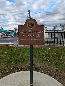 Sign in a park that reads "Anne Sullivan Memorial, Feeding Hills, Massachusetts, Funded by the Community Preservation Act Committee" beneath the Town of Agawam seal.