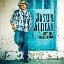 The cover consists of Aldean wearing a plaid shirt, denim jeans and cowboy hat standing behind a decrepit blue door.