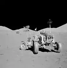 Black and white photo of a lunar rover with a lunar landing module in the background.