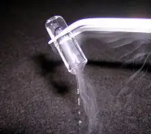 a glass tube, held upside down by some tongs, has a clear-looking ice-like plug in it which is slowly melting judging from the clear drops falling out of the open end of the tube