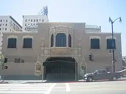 Color photograph of a two-story building. The main entrance has an awning and double doors. Above the entrance on the second story is an ornate bay window. On either side of the bay window there are smaller windows with balconets.