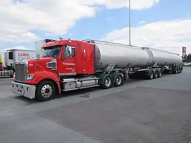 A red truck tractor pulling two silver oil tank trailers in tandem on a paved road.