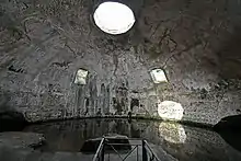 Bare concrete dome interior today called the Temple of Mercury with two square windows halfway up the dome on the far side, a circular oculus at the top, and a water level that reaches up to the base of the dome