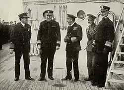 Five men, all in immaculate naval dress, stand on deck.