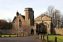 A gatehouse with a tower and a gateway to the right, all battlemented