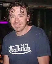 A man with short brown hair wearing a blue T-shirt with "Von Dutch" written on it