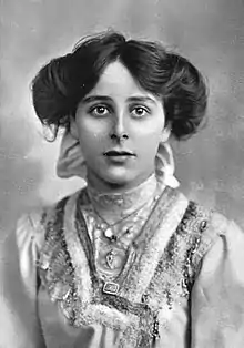 A young white woman with dark hair in an updo, full on the sides, wearing a gown with a high lace neck.