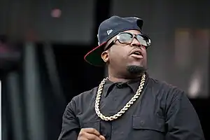 Big Boi dressed in black, with a gold chain and baseball cap turned sideways